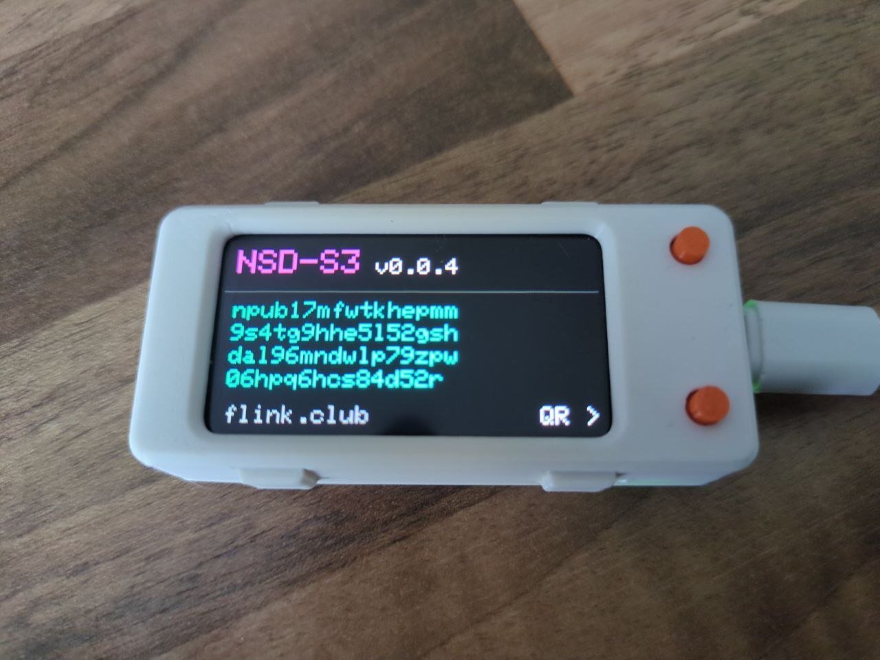NSD-S3 in its white case with orange buttons, screen showing the npub after flashing